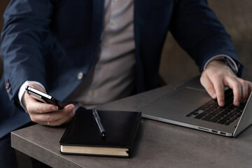 Businessman in suit sitting on orange sofa in office, talking on phone and using tablet and laptop....