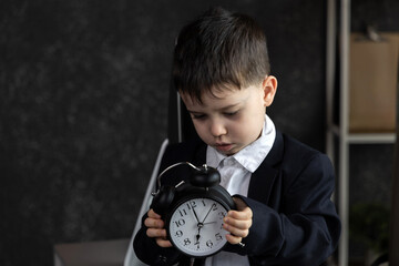 Funny baby boss in glasses sitting at desk with laptop, smartphone, and notebook. Child in suit...
