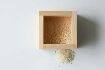 白背景に少しのコメが入った升とこぼれたコメ