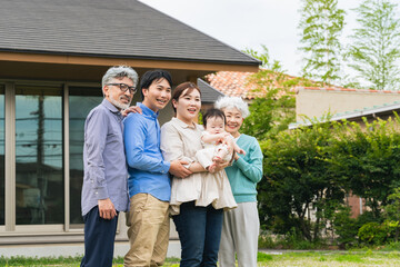 A group photo of a smiling three-generation family surrounding a baby in front of their home