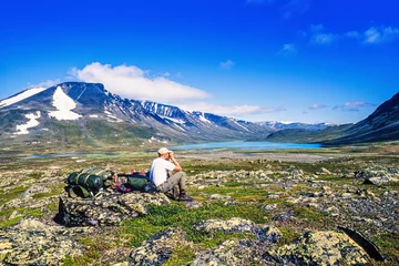 Gordijnen Hiker sitting and looking at a beautiful mountain landscape with a binoculars © Lars Johansson