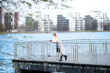 Woman enjoying a serene moment by the water while using her phone on a wooden deck surrounded by...