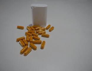 A group of capsules spilled next to a white plastic container on a plain background, highlighting...