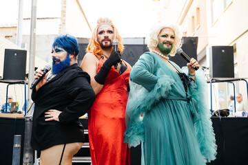 Bearded drag queens perform stand-up comedy at a lively outdoor event