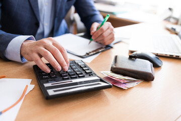 Man calculate domestic bills at home. Businessman using calculator at modern office. Young male checking balance and costs. Start up counting finance. Business people doing paperwork for paying taxes