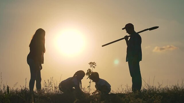 Family planting tree at sunset. Silhouette of parents and children work together growth hope for future generations. Tree planting highlights family bonds. Family tree planting silhouette at sunset.