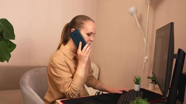 A focused young white woman is working on a computer at her desk. And he's on the phone. She takes the order by phone.