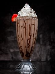 Chocolate milkshake served in a tall glass on a dark background. Isolated drink