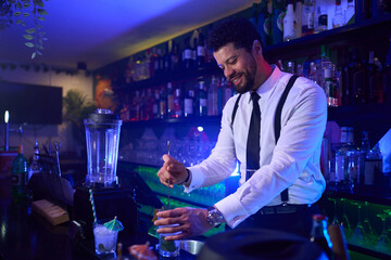 Bartender mixing cocktails in stylish bar with blue lighting