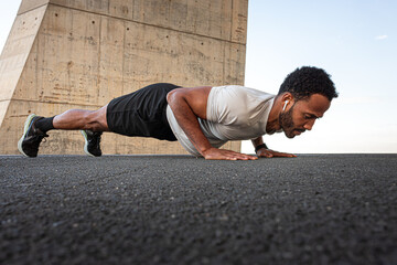 Determined black athlete doing push-ups outdoors in urban environment