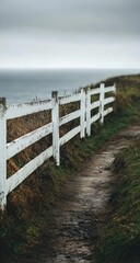 Obraz premium A weathered white fence lines a pathway at the edge of a misty ocean