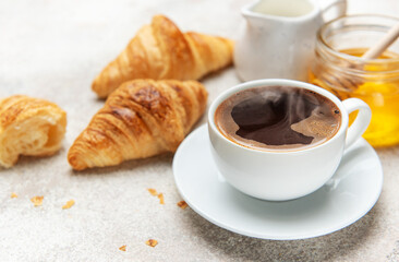 Steaming coffee, fresh croissants, and honey create a tempting breakfast scene