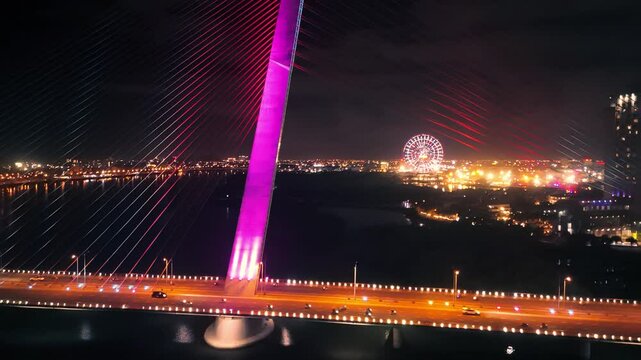 Nighttime traffic crossing brightly lit tran thi ly bridge, da nang cityscape with silhouetted ferris wheel glowing against dark sky