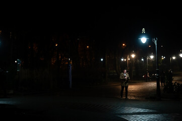 Under the dim streetlights, a lone figure enjoys a peaceful moment in the quiet park as night envelops the surroundings, inviting serenity in the city