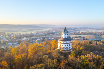 The elegant Baroque hunting chateau Humprecht stands above Sobotka, surrounded by vibrant autumn foliage, illuminated by the soft light of a tranquil sunrise. © pyty