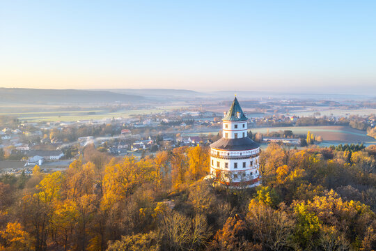 The elegant Baroque hunting chateau Humprecht stands above Sobotka, surrounded by vibrant autumn foliage, illuminated by the soft light of a tranquil sunrise.