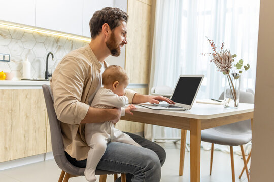 Self-employed young man working from home office while talking care of a baby