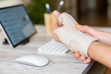 Employee wearing wrist support brace for thumb and wrist pain relief, suffering from rhizarthrosis, de quervain's tenosynovitis or carpal tunnel syndrome, working on computer at home office