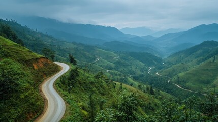 Fototapeta premium Winding road through lush green mountains under a cloudy sky. Perfect for travel blogs, promoting scenic drives, or adventure themes.