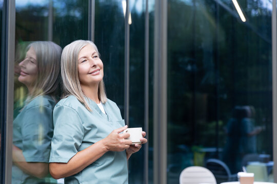 Mature caucasian female doctor having coffee and looking relaxed