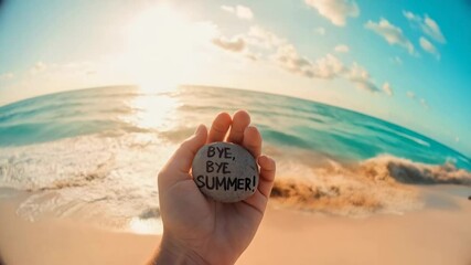 Warm sunset illuminating golden beach with hand grasping stone bearing farewell bye bye summer message against scenic coastal background
