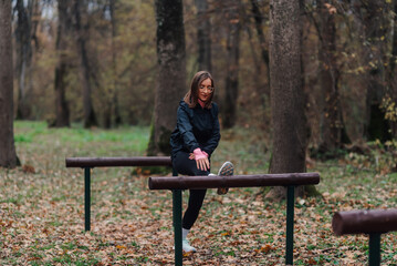 Woman stretching leg on wooden beam in autumn forest