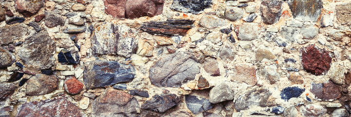 Ancient stone wall. Weathered rough masonry surface. The wall of the old castle. Wide panoramic texture for background and design.