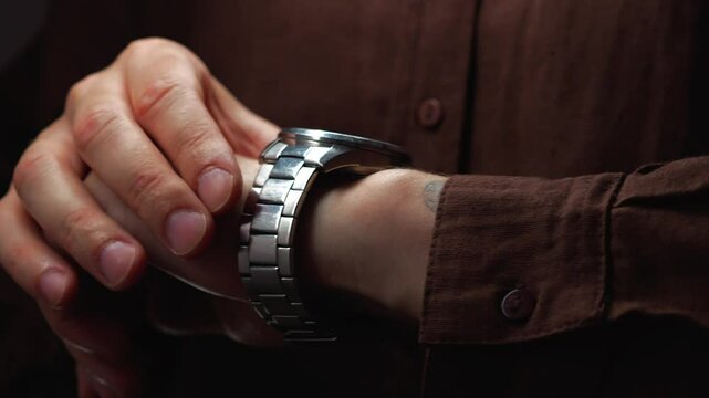 a watch with a snow strap on the hand of a man in brown clothes.
Stylish man with an elegant watch on his hand checks the time