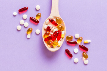 Vitamin capsules in a spoon on a colored background. Pills served as a healthy meal. Red soft gel vitamin supplement capsules on spoon