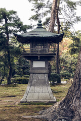 Aged Japanese lantern structure in a mossy garden setting with muted tones and soft lighting,...