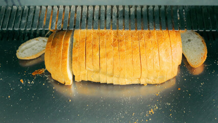 Freshly Baked Bread Loaf Being Sliced. A close-up of a freshly baked bread loaf being sliced by a bread slicing machine, with crumbs scattered around.