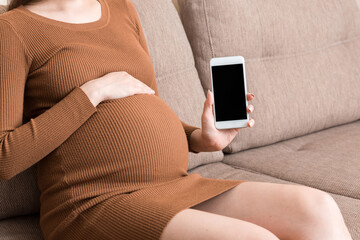 pregnancy with modern technologies.Pregnant woman showing cellphone with empty displayon sofa at...