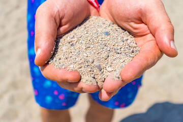 Close-up of male hands holding fine sand and pebbles on a sunny beach. Summer vacation concept,...