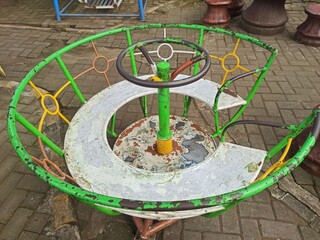 Vintage rusty playground merry-go-round with chipped paint and colorful metal bars. Old-school...