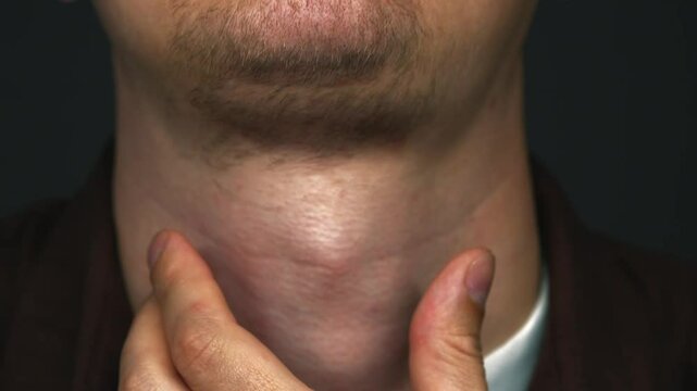 A man in a dark room swallows saliva.
Anatomy of the male body.
The Adam's apple moves when swallowing food.
Adam's apple on the neck