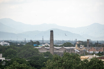 An expansive view of Madurai showcases industrial chimneys among lush greenery, with distant mountains