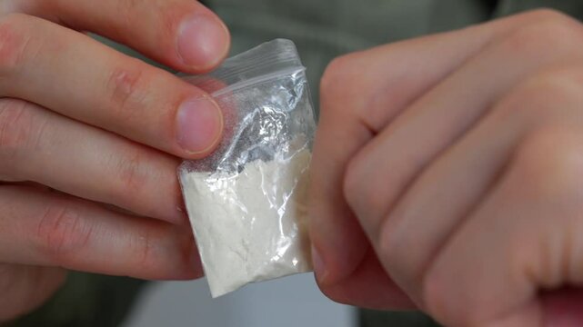 A man in a green shirt is holding a bag of drugs similar to heroin or cocaine.
White powder addict.
Drugs, harm, health, heroin