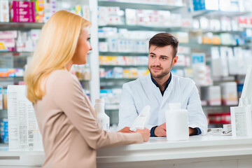 Pharmacist assists woman at pharmacy counter, offering medicine advice and friendly service – healthcare consultation and trust concept.