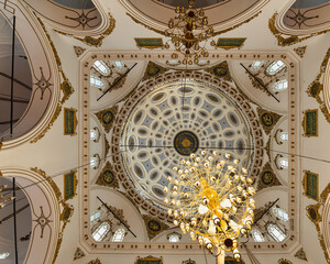 Gazing upwards inside Hisar Mosque in Izmir, Turkey, reveals a remarkable dome intricately decorated with patterns and golden accents, surrounded by elegant chandeliers