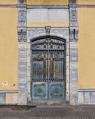 Architectural detail of ornate blue metal door with decorative ironwork, rust, and carved stone frame on yellow building