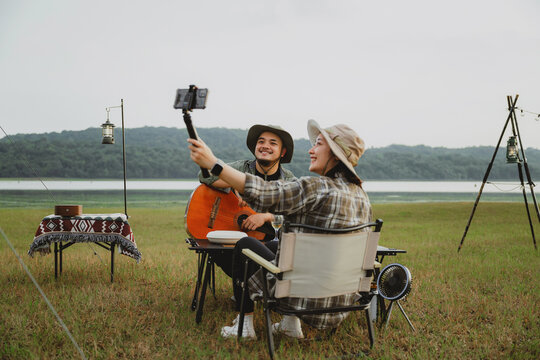 Young couple blogger enjoying outdoor lifestyle at tent site, Vlogging live scenic picnic moment with drinks and guitar music, Casual camping day with partner in nature, Relaxing in open field