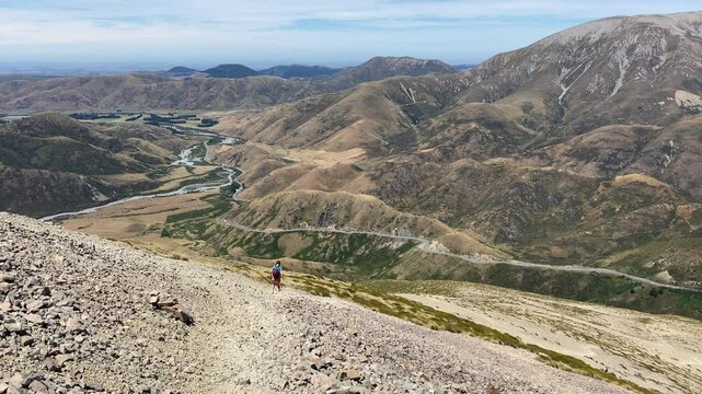 hiker girl walking on a rocky path from porters pass to foggy peak and castle hill peak; admiring stunning Lake Lyndon in torlesse tussocklands national park, canterbury, new zealand south island,