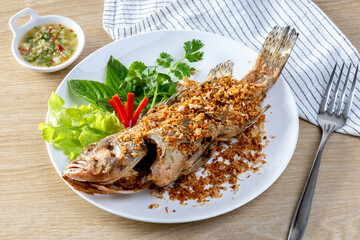 Fried sea bass sprinkled with Chinese garlic Fried until golden crisp, in a white dish,  on a  table.