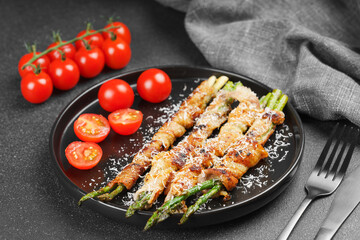 Grilled asparagus wrapped in crispy bacon sprinkled with parmesan cheese served on plate with fresh...