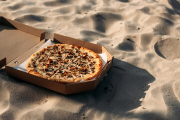Pizza in an open box resting on soft sand during golden hour. A quiet, tasty break under the...