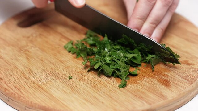Close-up of chef's hands skillfully chopping fresh parsley on a round wooden cutting board, preparing ingredients for a delicious culinary creation