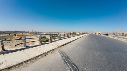 A wide, empty road with a clear blue sky, bordered by a metal railing and barren landscape. In Damascus Jobar district, Syria