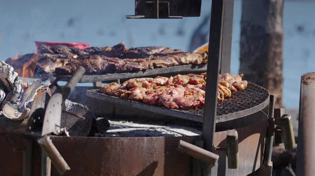 General still camera clip showing typical chinchulines and asado preparation over fire as person flips pieces with metal tong during sunny afternoon.