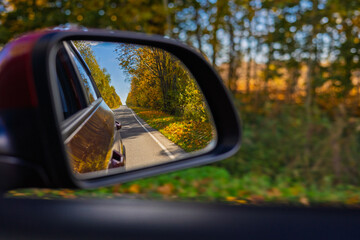 view in the rear view side mirror of a auto, driving a red car along the road
