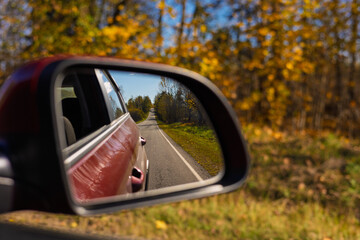 view in the rear view side mirror of a auto, driving a red car along the road